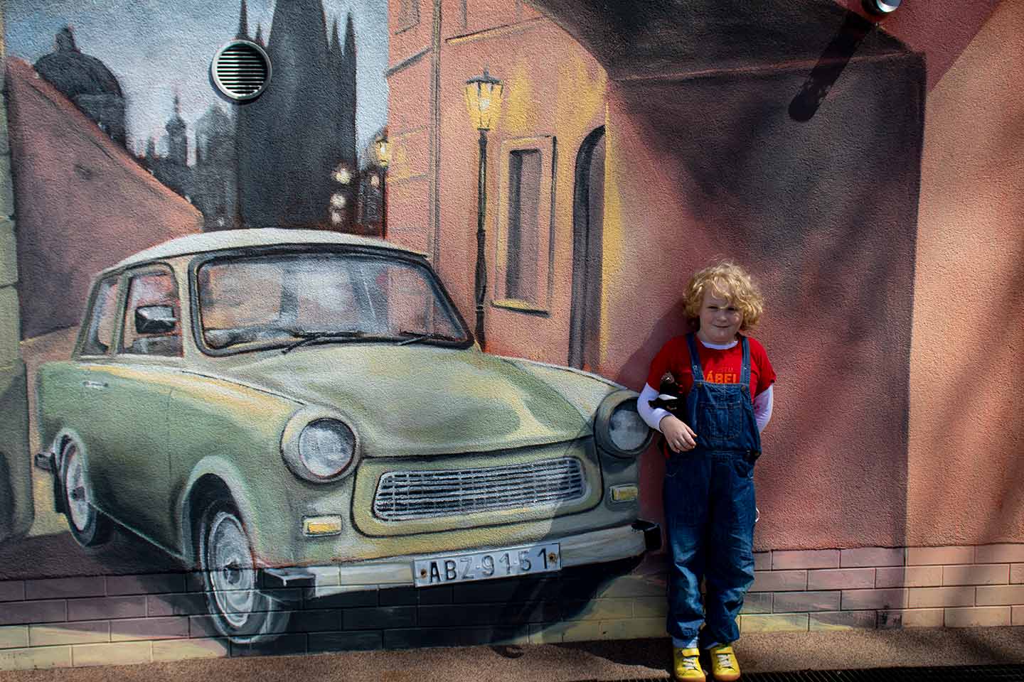Image of a child standing next to a mural at the Trabant Museum Prague