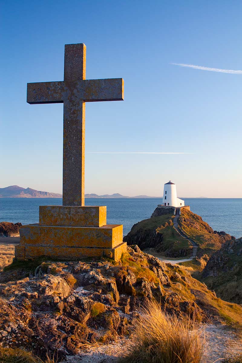 image of stone cross and lighthouse on Llanddwyn Island anglesey at sunset north Wales uk
