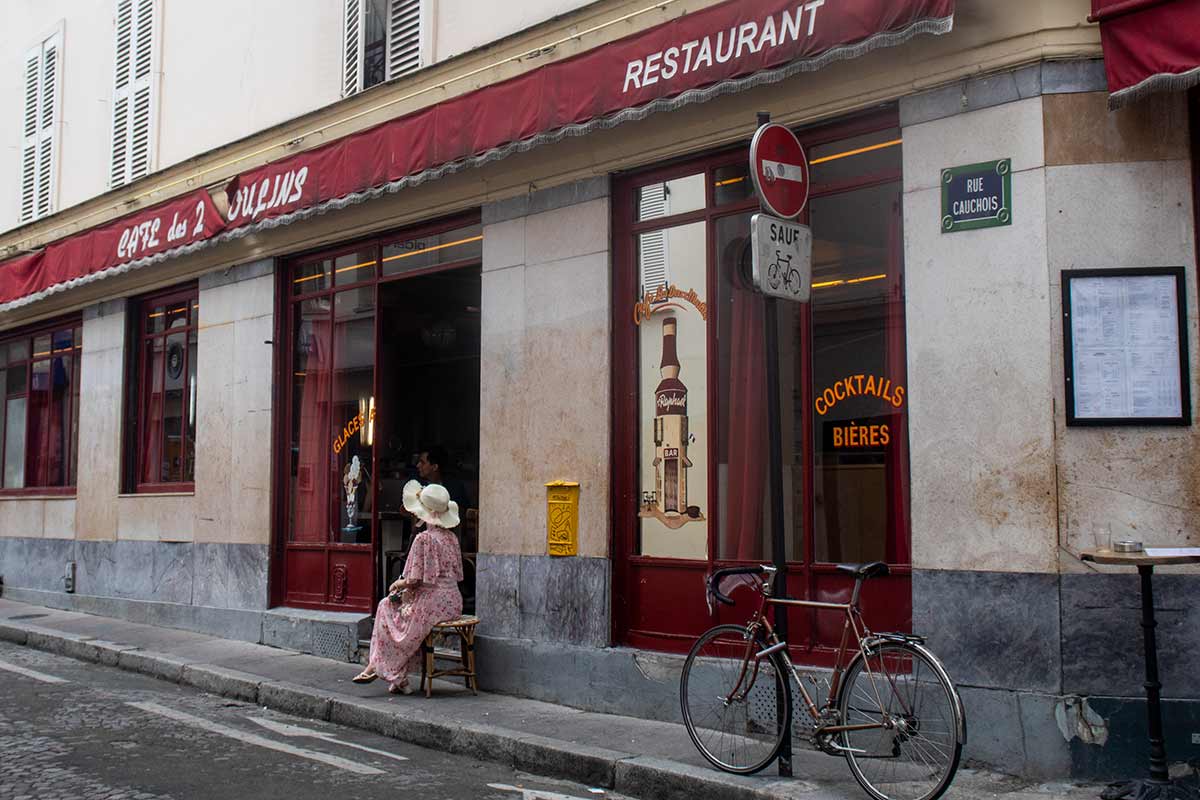 image of woman sitting outside cafe des Deux moulins Montmartre Paris france