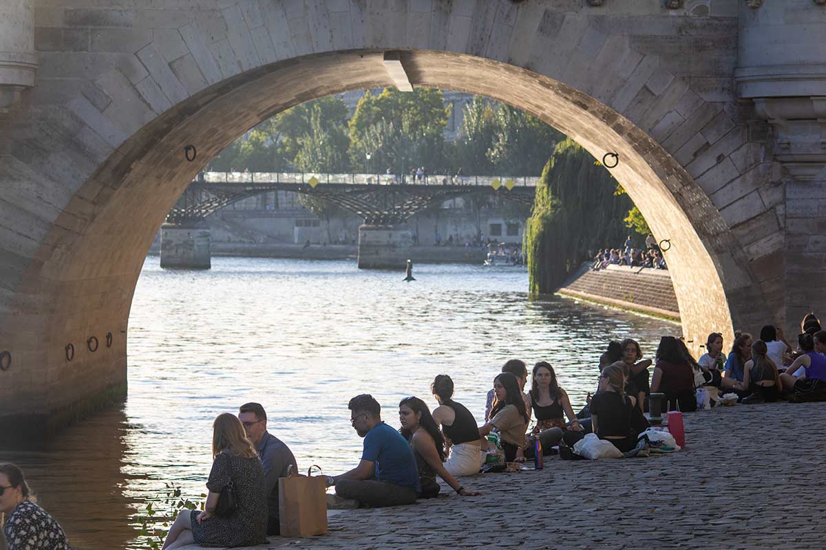 image of people sitting on the bank of the river seine below the pont nerf bridge Paris france